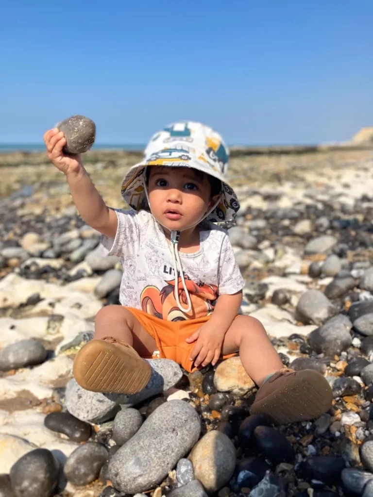 Child sat on a beach holding a pebble