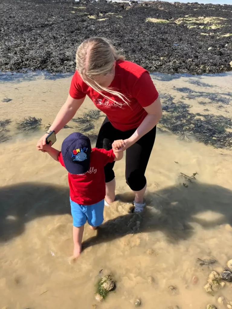 A child at the beach with an adult helping them walk in the sand